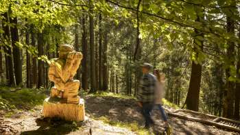 Hikers pass a carved figure with binoculars on the Walser Saga Trail