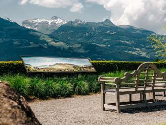 Wooden bench with a view of the Alps and a panoramic sign with mountain names in Vaduz, Liechtenstein