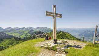Summit cross on Schönberg mountain with mountains and view of the Rhine valley in the background