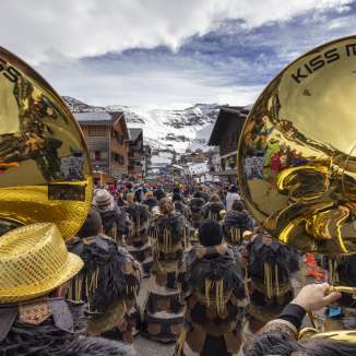 View of a Guggenmusik group with golden instruments at the carnival parade in Malbun against a snowy mountain backdrop.