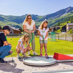 Family playing minigolf together in the sunny mountain village of Malbun in Liechtenstein - fun for young and old in the Alps.