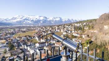 Telescope at the Schlossweg viewpoint Känzile with a view of Vaduz and the snow-covered Alpine panorama in the background.