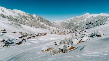 Aerial view of Malbun in winter with snow-covered wooden houses, nestled in the Liechtenstein Alpine landscape
