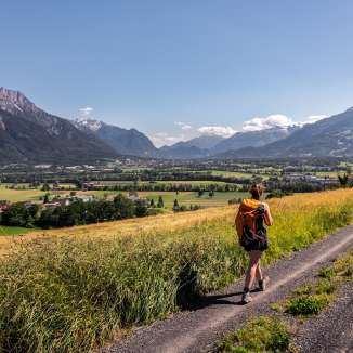Woman hiking on a dirt road with a panoramic view over the Rhine Valley in Liechtenstein