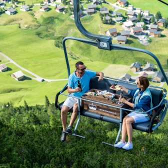 Two people enjoy a mountain breakfast in the pleasure chairlift with a view of the alpine village of Malbun in Liechtenstein