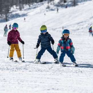 Three children learn to ski in the Malbun family ski area in Liechtenstein in sunshine and powder snow