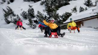Group of happy tobogganists on a groomed slope in Malbun, surrounded by snow-covered trees and alpine winter landscape