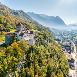 View of Vaduz Castle in Liechtenstein with autumnal colors, mountains and the Rhine Valley in the background
