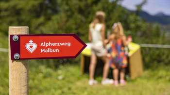 Signposts of the Malbun Alpine Heart Trail with children in front of one of the stations in the background