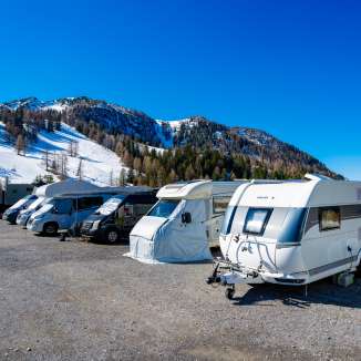 Motorhomes and caravans are parked on a snow-covered pitch in Malbun with a view of the Alps