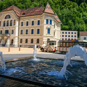 View of the government building in Vaduz with the Citytrain passing by and water fountains in the foreground