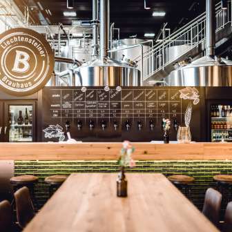 Interior view of the Liechtensteiner Brauhaus with gleaming brewing kettles, modern tapping system and cozy tasting counter with wooden tables