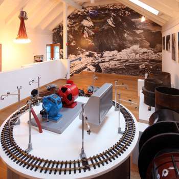 Model of a turbine on an exhibition platform in the Lawena Museum, with historical black and white photographs in the background.