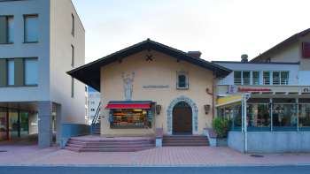 Exterior view of the Altes Kino Vaduz with lettering above the entrance and red awnings, located between two modern buildings.