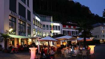 Evening atmosphere in front of the Brasserie Burg in Vaduz with illuminated terrace and guests under parasols.