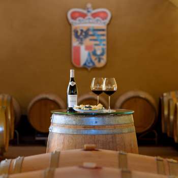 Wine barrel cellar with bottle of red wine and two glasses in front of the coat of arms of the Court Winery of the Prince of Liechtenstein