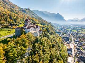 View of Vaduz Castle in Liechtenstein with autumnal colors, mountains and the Rhine Valley in the background