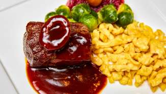 Delicious game dish with dark sauce, golden yellow spaetzle, Brussels sprouts and cranberries served on a white plate.