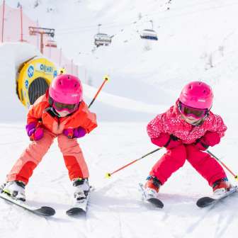 Two children with pink helmets are skiing on the slopes in Malbun in the sunny winter weather, laughing.