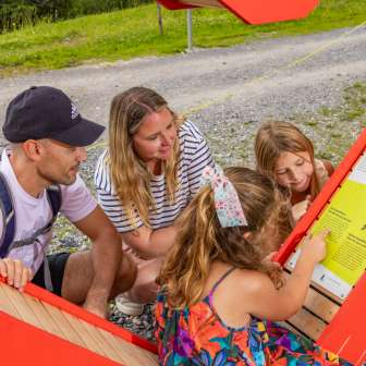 Family with children eagerly reading the information board on the Alpine Heart Trail in Malbun, an interactive hiking trail in the mountains of Liechtenstein.