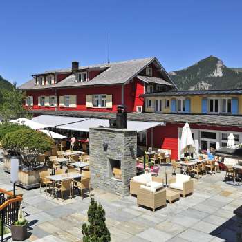 Exterior view of the restaurant in the sunshine, with red façade and mountainous panorama.