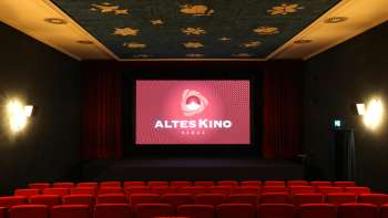 Cinema auditorium of the Altes Kino Vaduz with red cinema seats, a stage with a red curtain and a blue ceiling with golden star motifs.