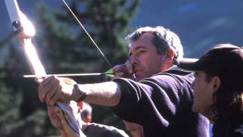 A man concentrates on drawing a bow during archery in Malbun while a guide stands by his side - an exciting outdoor experience in the middle of the mountains.