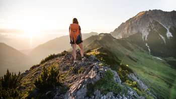 Hiker with rucksack standing on a mountain ridge in Liechtenstein and gazing into the rising sun.