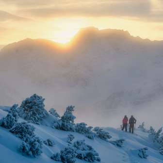 Two people, including Tina Weirather, hike through a snowy winter landscape at sunset in the mountains of Liechtenstein.