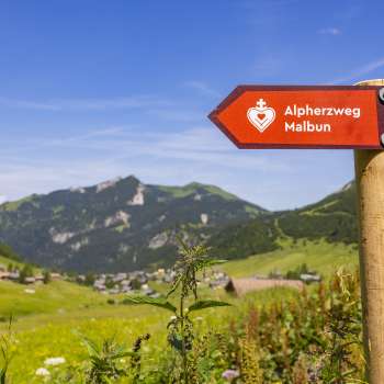 Alpine Heart Trail signpost with the mountain village of Malbun in the background