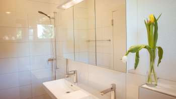 Modern, brightly tiled bathroom in the guest house at Camping Mittagsspitze with double washbasin, mirror and fresh flowers.