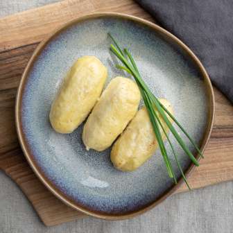 Three Hafalääb dumplings on a plate with chive garnish, served on a wooden board - a traditional dish from Liechtenstein