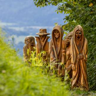 Detailed view of carved wooden figures in mystical depiction on the Walser Legend Trail in Triesenberg, surrounded by green nature