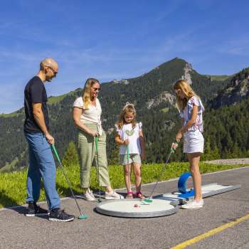  Family playing minigolf together in the mountains of Malbun in bright sunshine