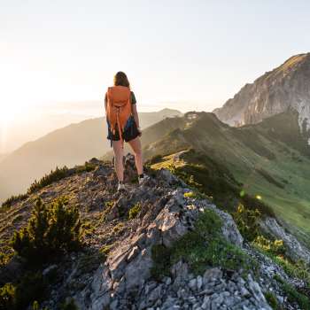 Hiker with rucksack standing on a mountain ridge in Liechtenstein and gazing into the rising sun.