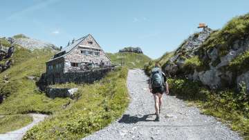 Woman with backpack on a mountain trail just before the Pfälzerhütte hut alpine backdrop, marked hiking route, and green high mountain meadows