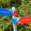 Colorful signpost of the Liechtenstein Trail with red and blue arrows against a green forest background