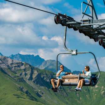 Two people enjoy breakfast on the pleasure chairlift in Malbun with an impressive mountain backdrop
