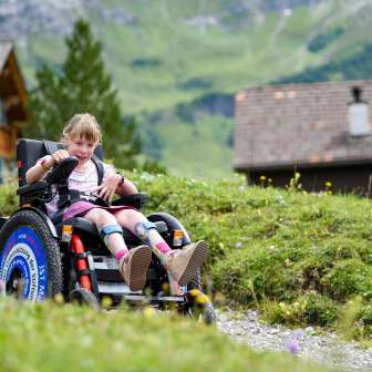 Girl in an electric wheelchair on a hiking trail in Malbun with a green mountain backdrop.