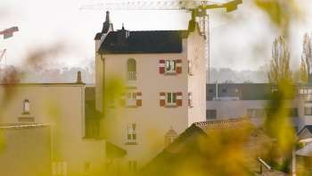 Close-up of the historic tower of Vaduz Town Hall with striking red shutters, surrounded by construction site cranes in the background.