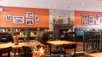 A cozy dining room at New Castle Restaurant, featuring warm colors, a fireplace, and stylish wooden tables