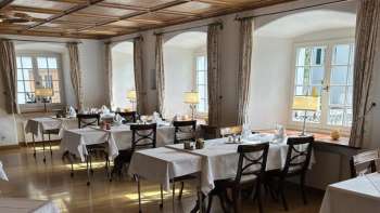 Bright, classic dining room with white tablecloths and wooden floor.