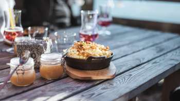 Regional specialty "Käsknöpfle" with apple sauce on a wooden table in front of an alpine backdrop