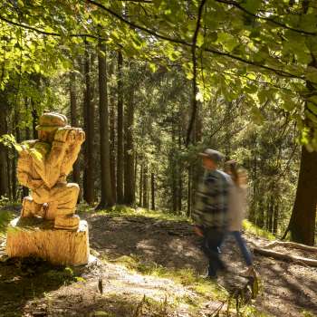 Hikers pass a carved figure with binoculars on the Walser Saga Trail