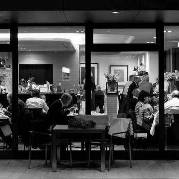Black and white photo of a busy restaurant with a view from outside through the glass front.