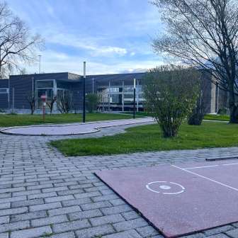 Minigolf course with several holes on a well-tended green area between Schaan and Vaduz, with modern buildings and trees in the background.