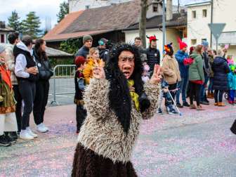 Disguised Schaan witch at the carnival parade in Schaan, Liechtenstein, in front of an audience and colorful confetti on the street