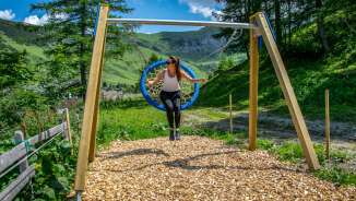 Woman swinging on a nest swing in Malbun, Liechtenstein, surrounded by mountains, meadows and summer nature