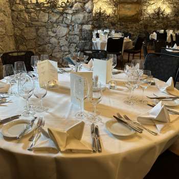 Elegantly laid round table with white tablecloths, napkins and menus in front of a stone wall.