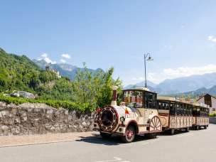 Citytrain passes through Vaduz, in the background Vaduz Castle and the Alps in bright sunshine